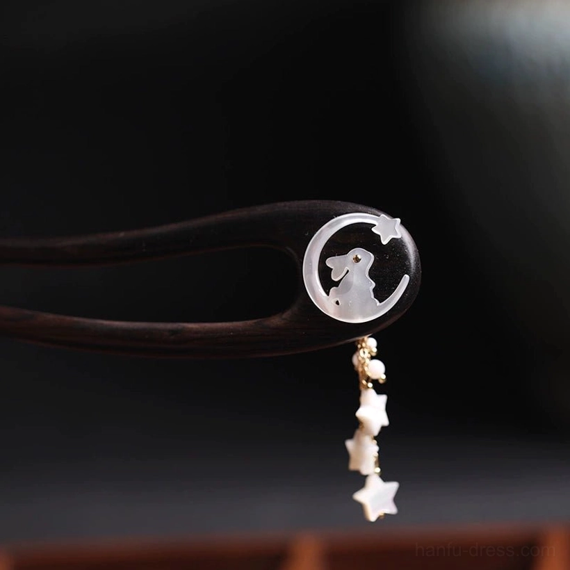 Close-up of a double-pronged Moon Rabbit Chinese hair stick with dark wood body, mother-of-pearl moon rabbit inlay, and star tassel