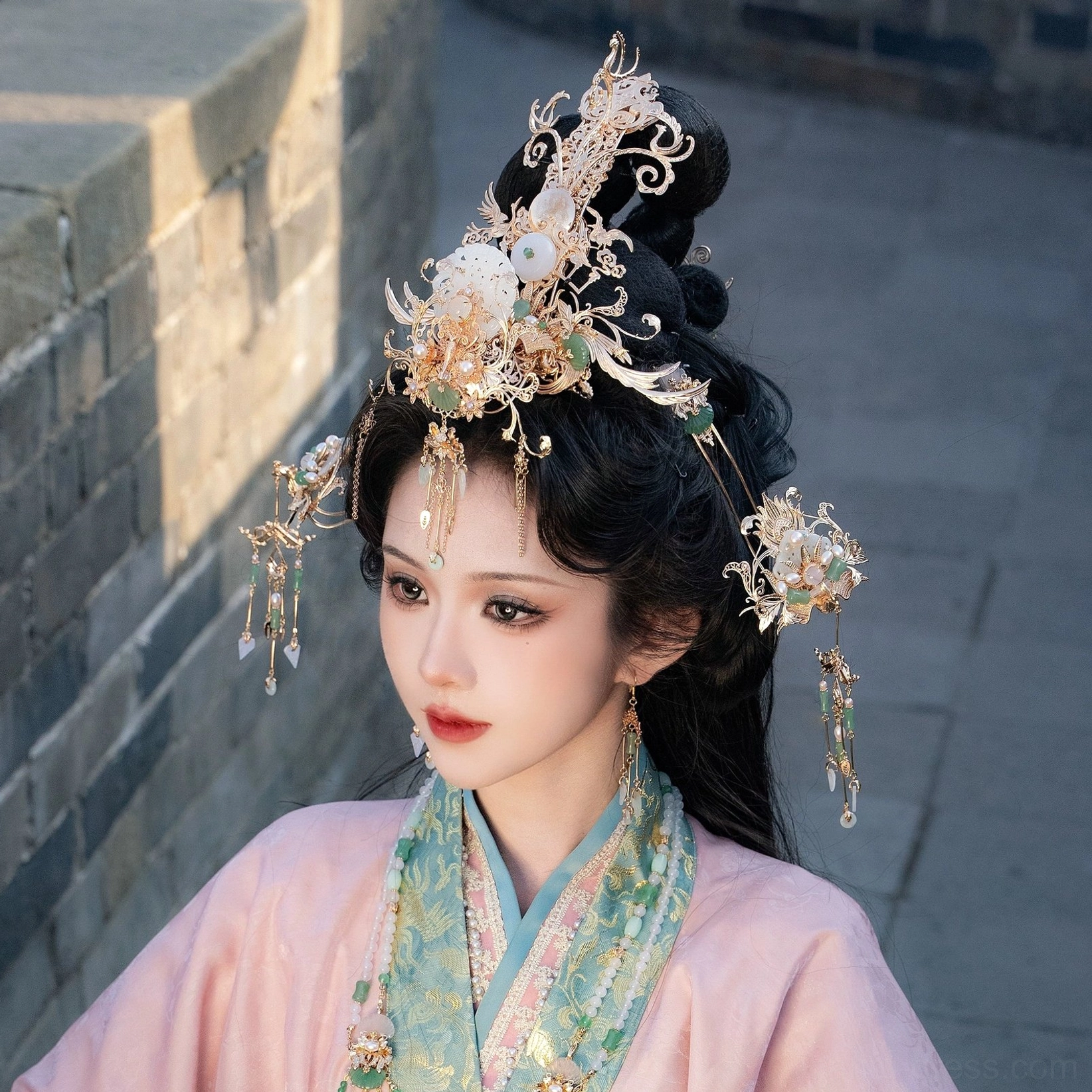 Model wearing a complete Moon Shadow Chinese hanfu hair accessories set with gold filigree crown jade-inspired ornaments and tassel hairpins with pink hanfu at an ancient city wall