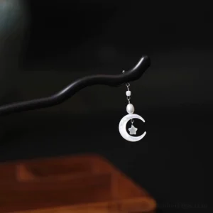 Close-up of moon and star Chinese hair stick with a dark wavy shaft, pearl beads, and crescent moon pendant on a wooden tray