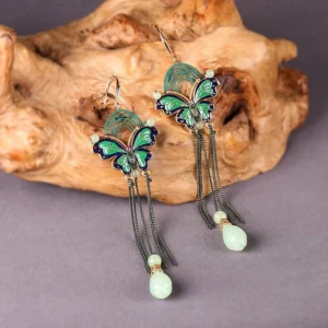 Green blue enamel butterfly teardrop fringe earrings with black chain tassels and light green jade style pendants displayed on a purple background