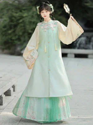 Mint green Ming Dynasty Hanfu set with cream robe, bijia vest, floral embroidery and printed pleated skirt photographed in a garden