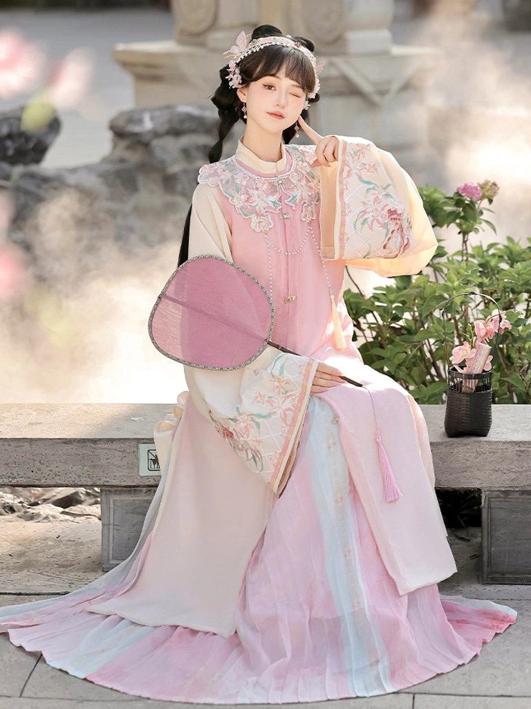 Seated model wearing pastel pink Ming style Hanfu with floral hair ornament, cloud collar and gradient pleated skirt in a courtyard