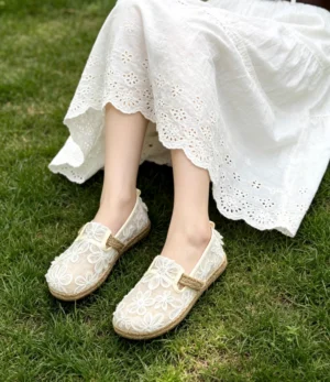 Off-white floral lace Chinese Hanfu slip-on shoes styled with a white embroidered dress on grass, featuring round toes and espadrille jute-look trim