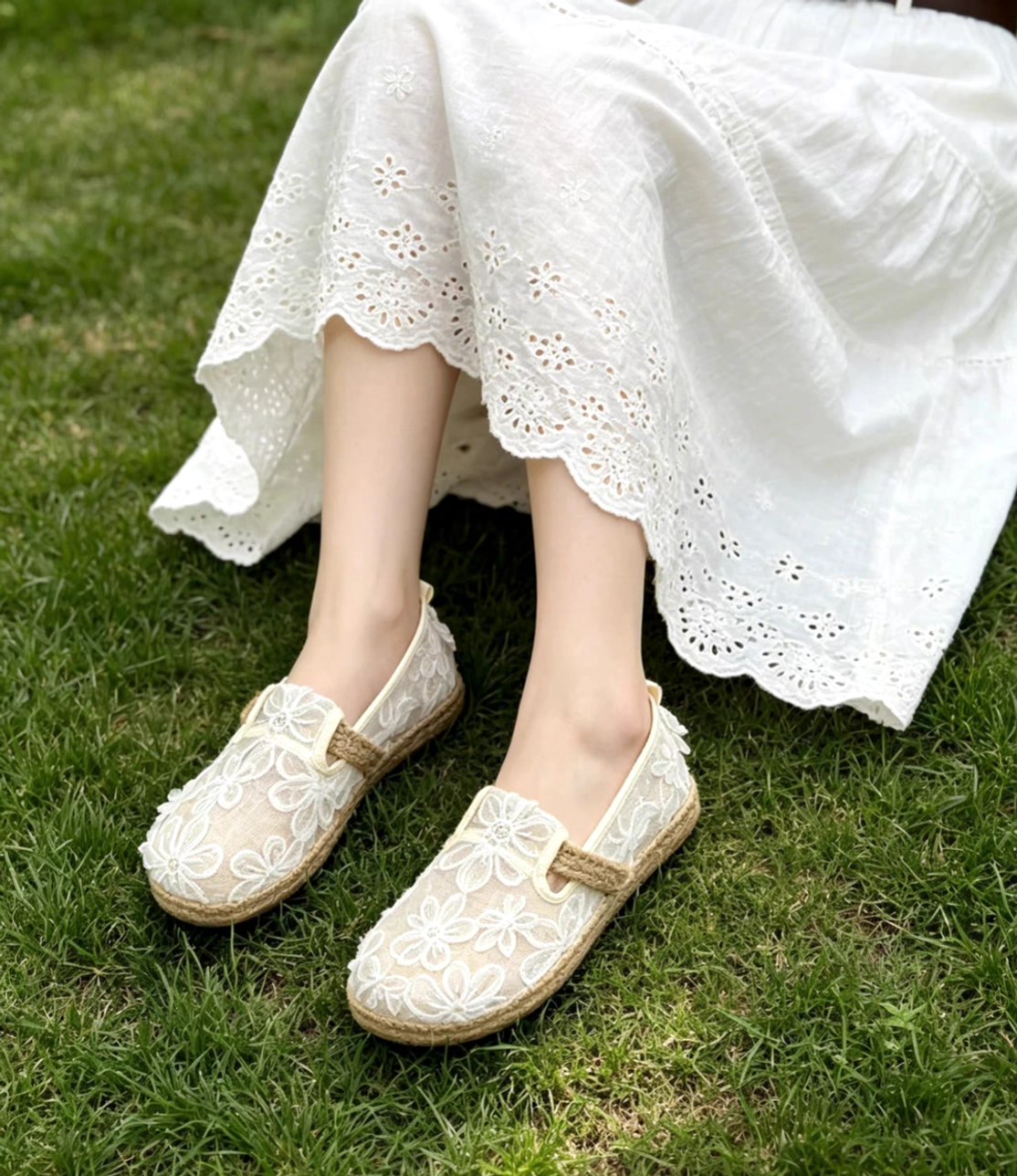 Off-white floral lace Chinese Hanfu slip-on shoes styled with a white embroidered dress on grass, featuring round toes and espadrille jute-look trim