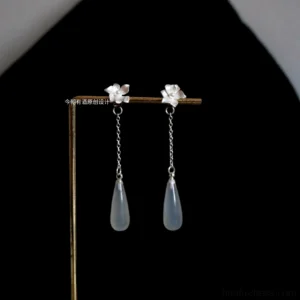 Floral Hanfu dangle earrings with silver flower studs, delicate chains, and opaque light blue teardrop pendants displayed on a gold jewelry stand against a black background