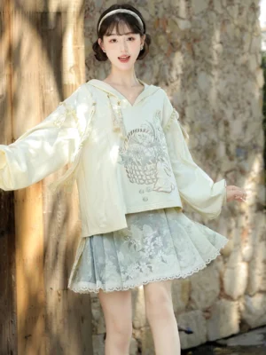 Front view of cream embroidered hooded Hanfu crop top with tassel sleeves and sage green short horse face skirt
