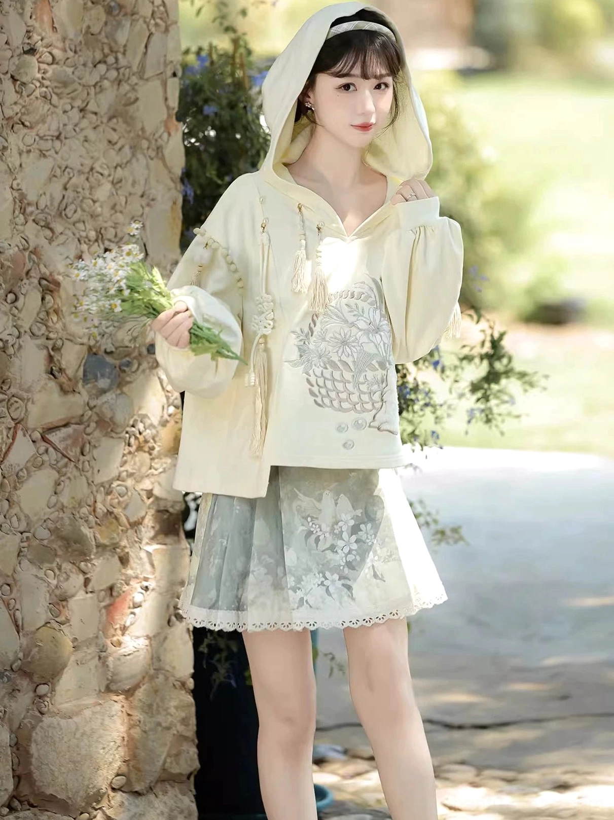 Modern Hanfu two piece outfit with hood worn up featuring cream tassel hoodie and short sage mamianqun skirt