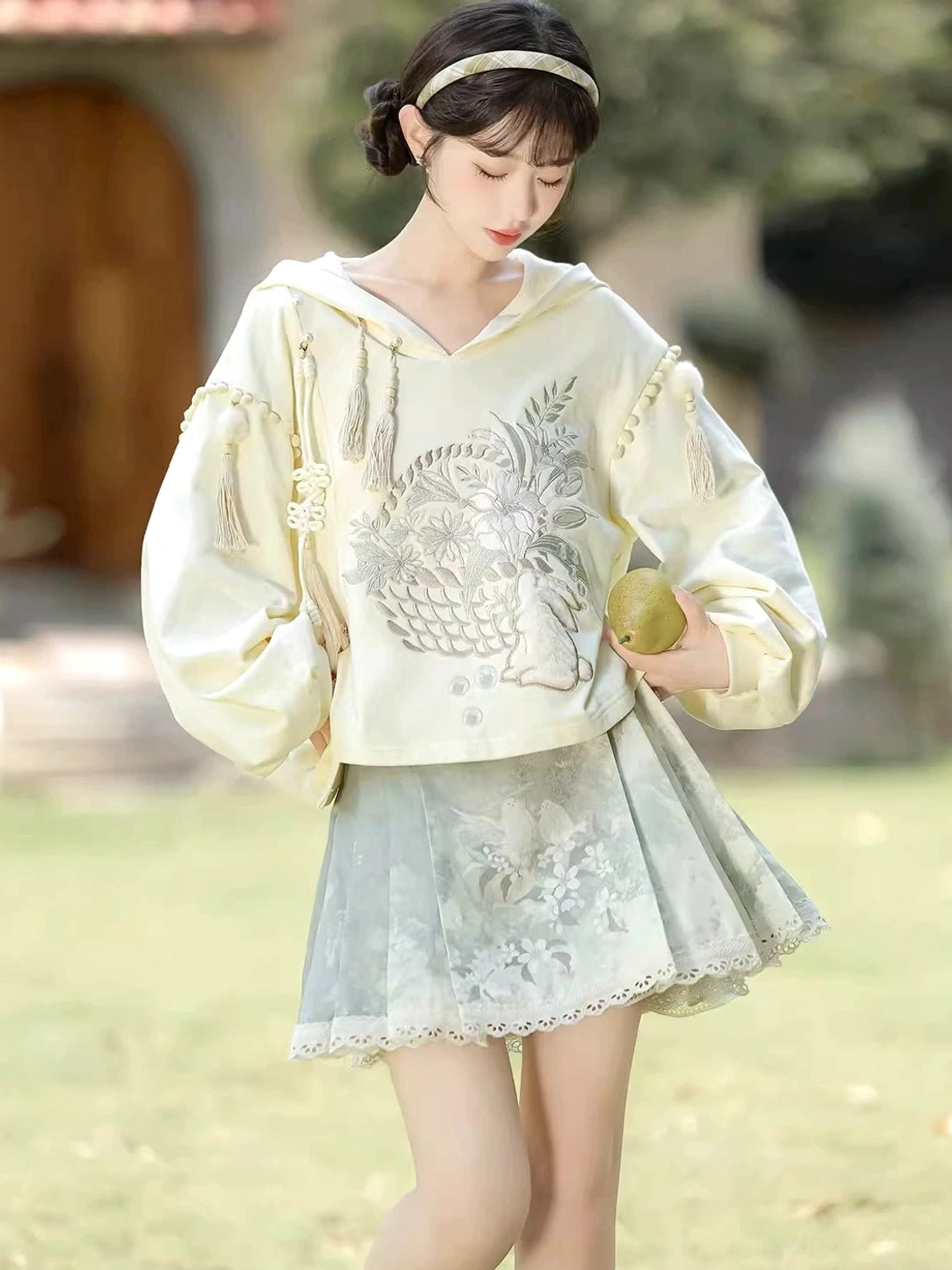 Side front full body view of the sage green pleated horse face skirt and cream modern Hanfu hoodie outfit
