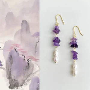 Asymmetrical amethyst freshwater pearl drop earrings with gold hook ear wires arranged on a Chinese ink wash mountain landscape background