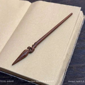 Reddish-brown carved wooden spear hair stick with traditional cloud motifs displayed on an open kraft paper notebook