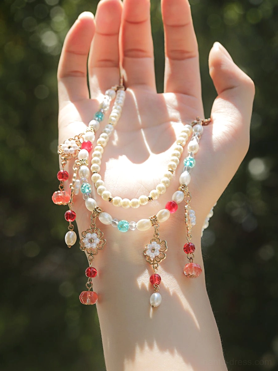 Multi-layered Chinese vintage necklace shown across a hand, featuring assorted bead strands, gold filigree flowers, freshwater pearls, red and turquoise charms, and dangling pendants