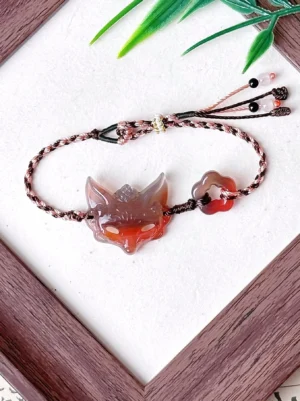 Adjustable natural agate fox spirit bracelet showing carved fox charm, flower agate accent, braided tassel ends, glass bead details, and decorative metal bead