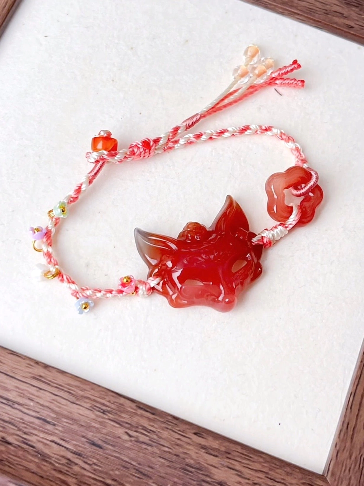 Natural agate fox spirit bracelet shown from above with carved fox head pendant, mixed colorful beads, red cylindrical bead, adjustable braided cord, and tassel ends