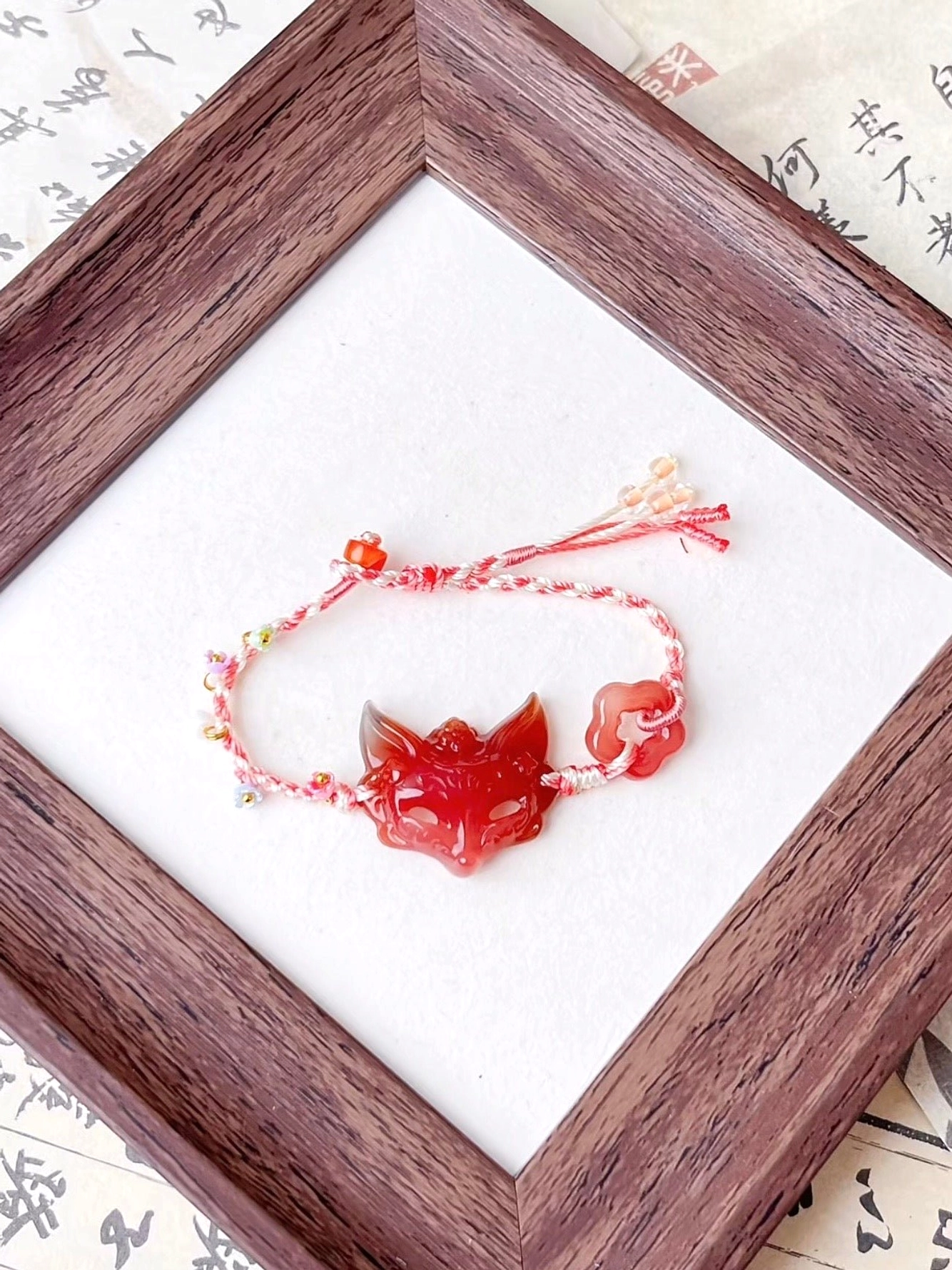 Red agate fox spirit Chinese bracelet with hand-braided pink and white cord, colorful beads, carved fox pendant, cloud charm, and vintage Chinese calligraphy background
