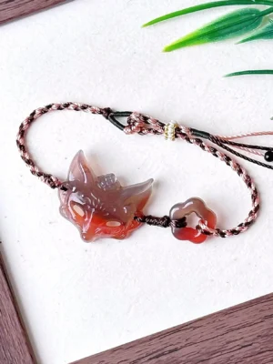 Natural agate fox spirit Chinese bracelet with carved fox mask charm, flower-shaped agate bead, and hand-braided brown pink and ivory cord displayed on a white background