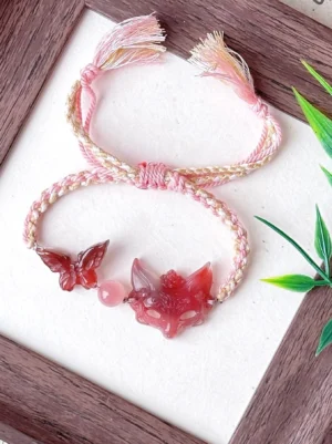 Natural agate fox spirit Chinese bracelet with hand-braided pink ivory and gold cord, red agate butterfly, carved fox pendant and decorative tassels displayed with bamboo leaves