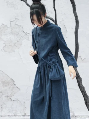 Three-quarter view of a navy blue Chinese-inspired long-sleeve cheongsam dress with flowing maxi skirt, relaxed silhouette, and softly textured fabric