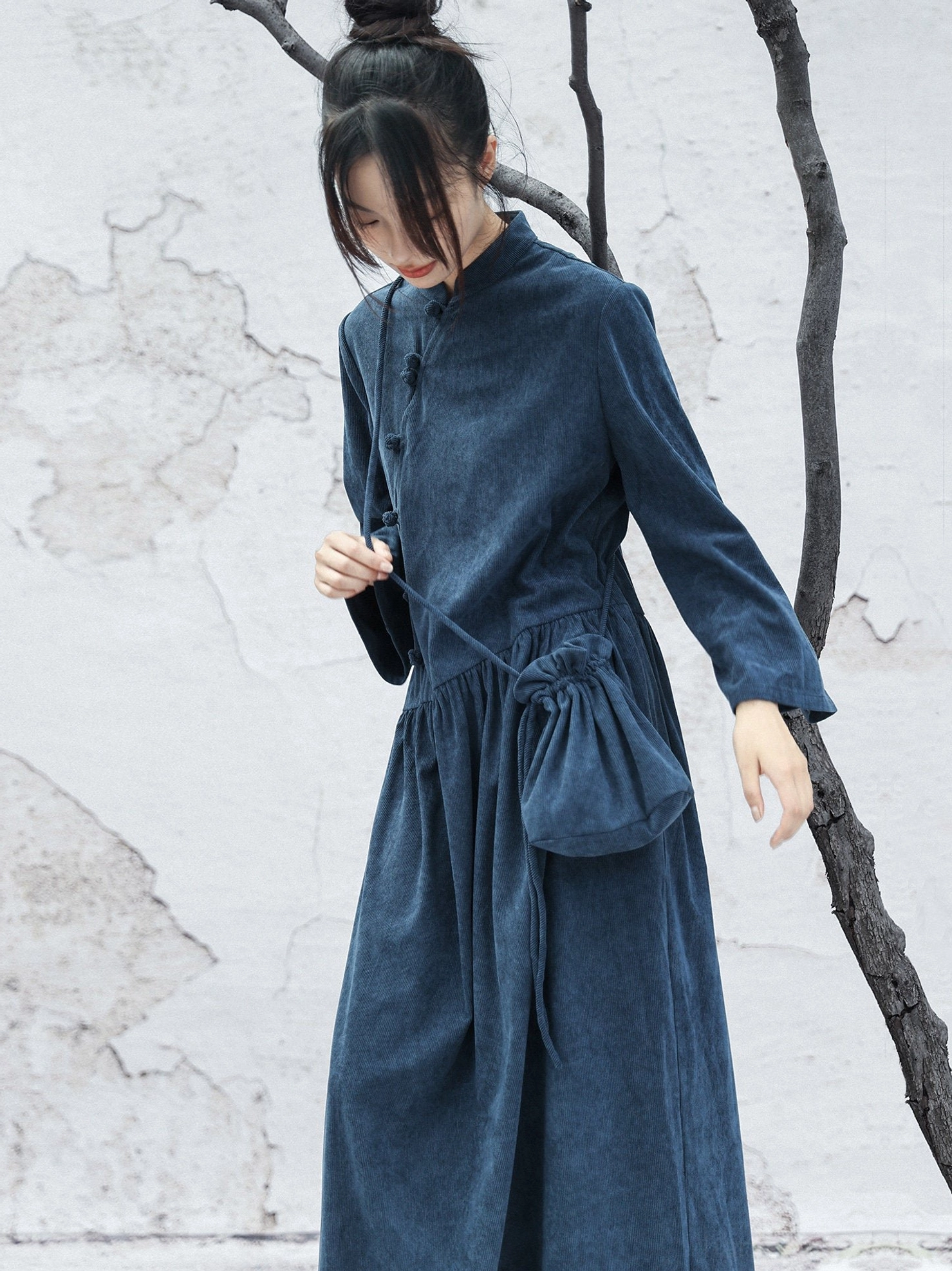 Three-quarter view of a navy blue Chinese-inspired long-sleeve cheongsam dress with flowing maxi skirt, relaxed silhouette, and softly textured fabric