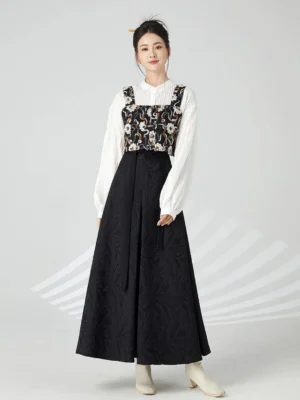 Front full-body view of a woman wearing a Ming-inspired modern Hanfu outfit with white stand-collar puff-sleeve blouse, floral jacquard bustier, black long skirt, and beige ankle boots