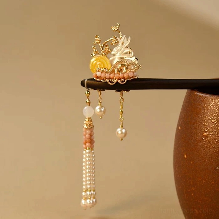 Nine-tailed fox Chinese hair stick with black wooden pin, white shell fox carving, gold filigree, pink beads, pearls and flowing tassels beside ceramic jar