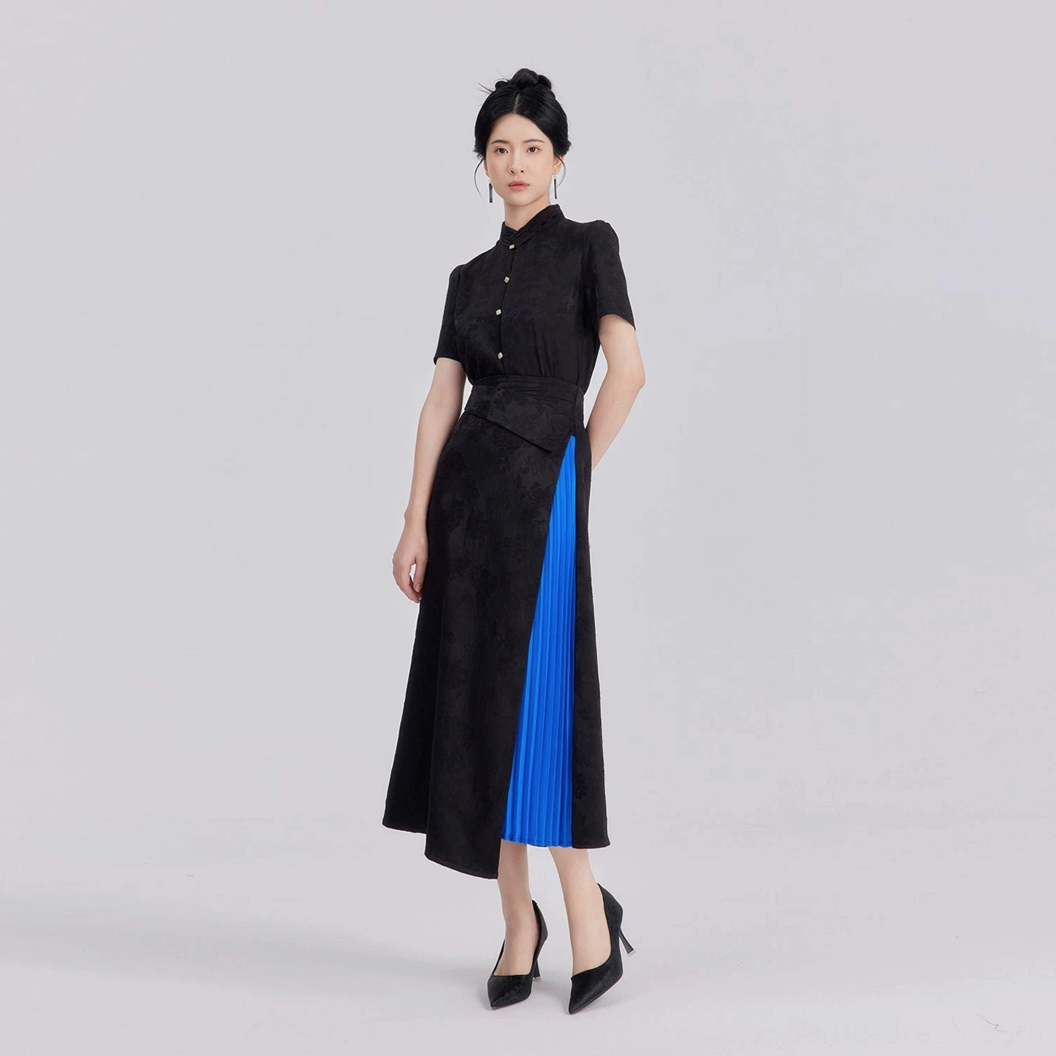 Full-body view of woman wearing coordinated Nocturne modern Hanfu black jacquard shirt and asymmetrical skirt set with blue pleated accent