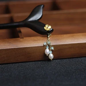 Decorated dark mermaid tail Chinese hair stick with golden floral ornament, pearl-like beads, and tassel displayed on a wooden tray