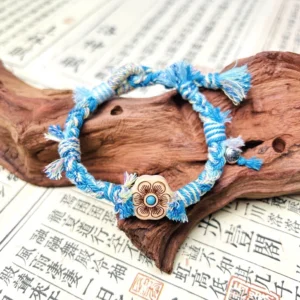 Ocean blue handwoven Tibetan knot Chinese bracelet with blue braided cords plum blossom wooden charm tassels and small bell on calligraphy paper