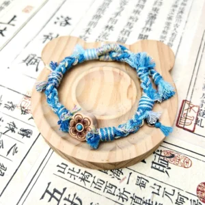 Top view of blue and green Tibetan-inspired handwoven Chinese bracelet with plum blossom charm frayed tassels and metal hanging ornament
