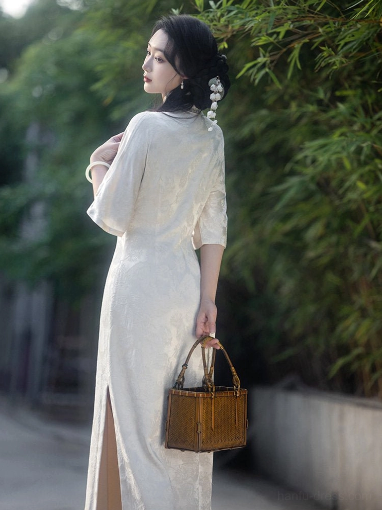 Back three-quarter view of an off-white floral jacquard qipao dress with stand collar, long silhouette, side slit hem, and traditional Chinese styling