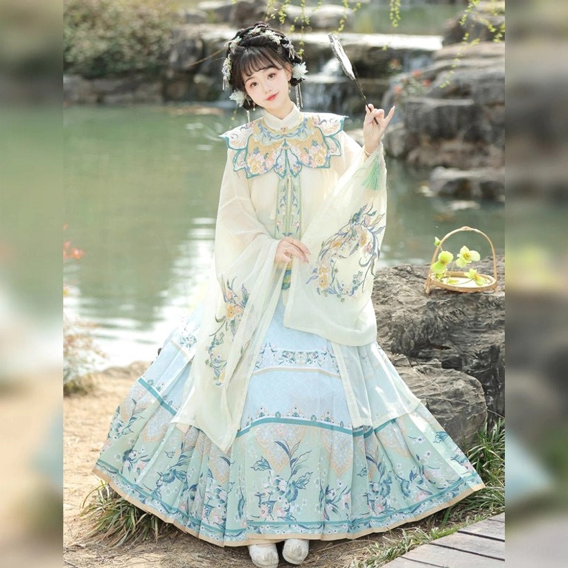 Off-white and light blue Ming Dynasty Hanfu set with full embroidered mamian skirt, elegant robe, feather fan, and wicker basket in a lakeside setting