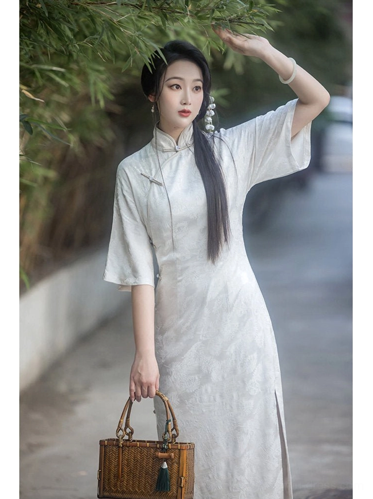 Off-white retro Chinese style cheongsam dress with stand Mandarin collar, half flare sleeves, full-length silhouette, and woven bamboo handbag