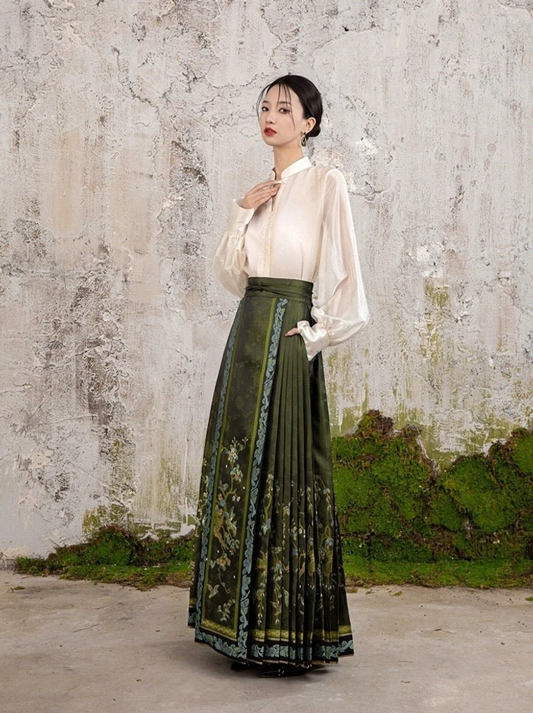 Side profile of an olive green Ming style mamianqun with long pleated silhouette, floral embroidered front panels, decorative trim, and high waistband