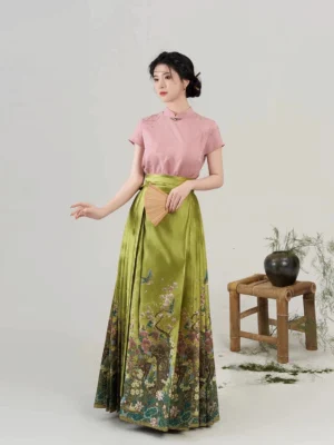 Side three-quarter view of an olive green pleated mamian skirt with garden floral print, styled with a pink Chinese blouse and traditional folding fan