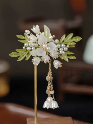 One-leaf lily vintage Chinese hair pin displayed on a metal stand, showing white floral decorations, green leaves, pearl accents, and hanging golden lily pendants