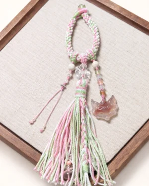 One-of-a-kind pink agate fox spirit Chinese keychain with pink green braided cord clear beads and two-tone tassel displayed on a wooden tray
