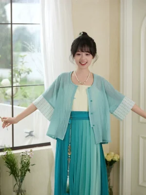 Modern Hanfu three piece outfit with cyan Ming style blouse ivory camisole teal pleated skirt and waist tassel by window
