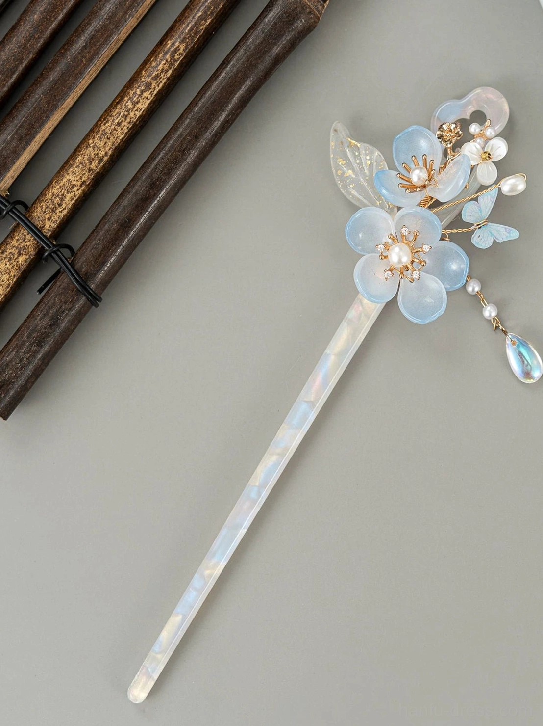 Top view of opalescent Chinese hair stick with blue resin flowers, leaf ornaments, pearl-like details, and blue dangling tassel