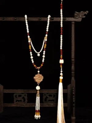 Traditional Chinese Hanfu long tassel pendant necklace displayed on a carved wooden jewelry stand, featuring layered white red and amber beads, a carved bronze Ruyi pendant, and flowing silk tassels