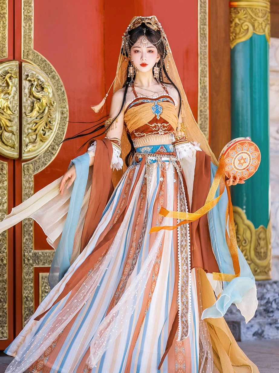 Front view of the orange Dunhuang Feitian Hanfu colorway with brown, cyan, and terracotta tones, halter camisole, gemstone-style ornament, and flowing silk scarves beside a red wooden door