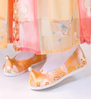 Orange embroidered upturned-toe Hanfu shoes for women worn with a gradient traditional Chinese Hanfu skirt and white socks, featuring floral cloud embroidery, pearl toe decoration, and white rubber soles