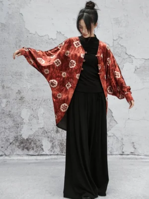 Side front view of a Chinese-inspired orange-red velvet bat-sleeve jacket showing the flowing oversized sleeves, frog-button placket, and relaxed modern Hanfu silhouette