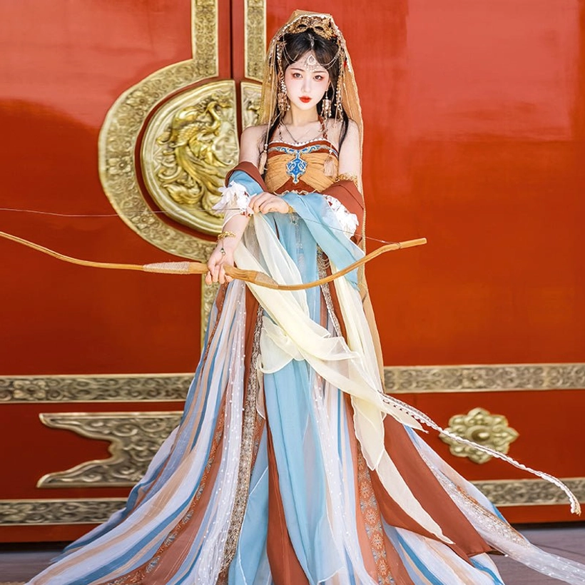 Front view of orange and terracotta Dunhuang Feitian Hanfu costume with embroidered halter top, long pleated skirt, layered silk accents, and traditional bow beside an ancient red wooden door