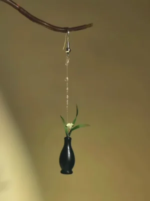 Single orchid in vase dangle earring with white flower green leaves black vase and silver hook displayed on a twig