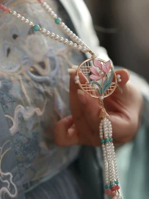 Orchid yingluo Chinese necklace worn with light blue embroidered Hanfu, featuring pink floral pendant, pearl chain and green tassels