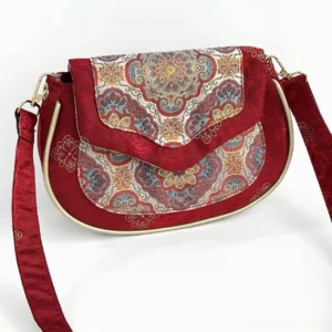 Three quarter view of an oriental Chinese brocade crossbody bag with wine red embroidered panels, elegant flap closure, gold border trim, and adjustable jacquard shoulder strap