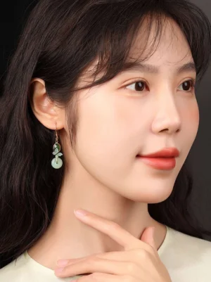 Oriental Chinese butterfly jade earrings worn on the ear with green pendants and golden details styled against an elegant neutral outfit
