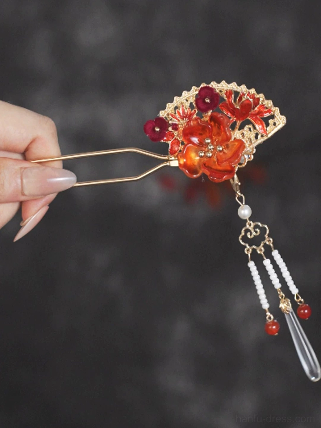 Hand holding oriental flame fan Chinese hair stick showing double prongs red floral fan ornament and cascading bead tassels