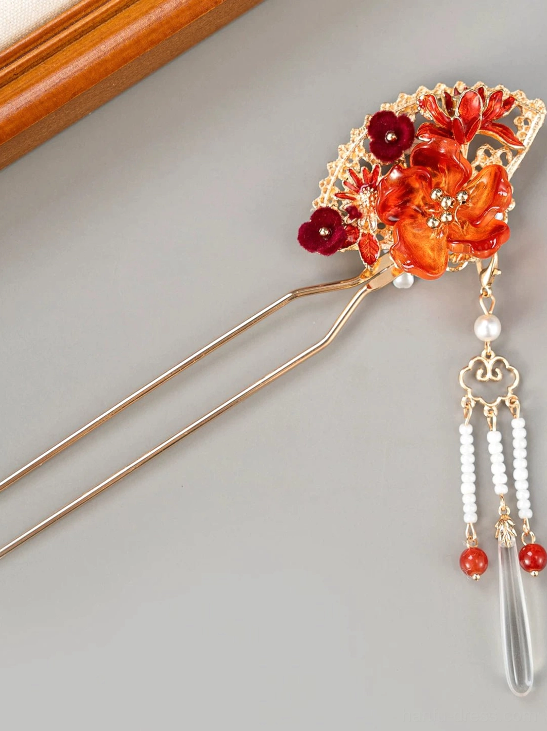 Front angled view of gold tone fan shaped Chinese hair stick with red floral ornament hanging bead tassels and teardrop charm