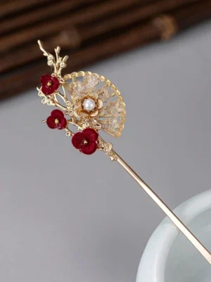 Oriental plum blossom fan Chinese hair stick with red velvet flowers, gold-toned filigree, pearl center, and crystal embellishments displayed on a bamboo mat