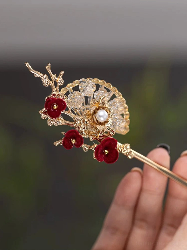 Oriental plum fan Hanfu hair accessory held in hand showing the polished gold hair shaft, red plum blossom decoration, pearl, and crystal fan details